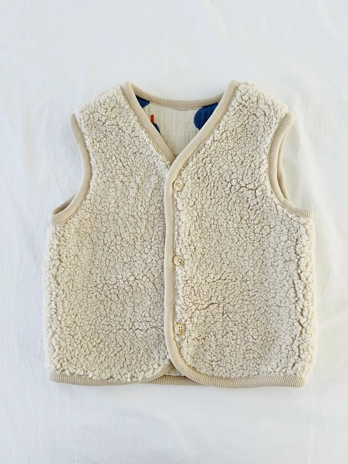 Gilet sans manches en sherpa écru avec trois boutons beiges et bordure côtelée beige, côté sherpa