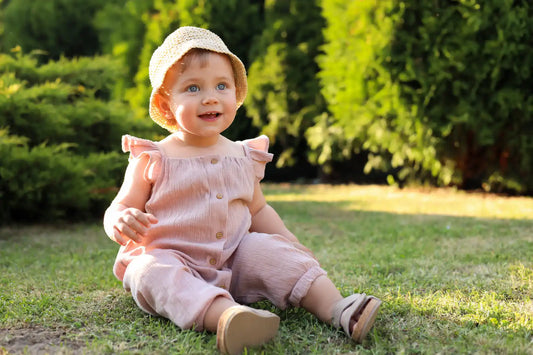 Bébé fille en combinaison gaze de coton rose et chapeau de paille assise dans un jardin