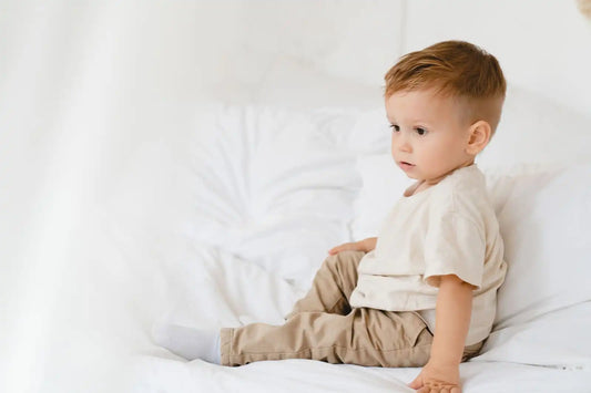 Enfant en tenue beige en coton assis sur un lit blanc