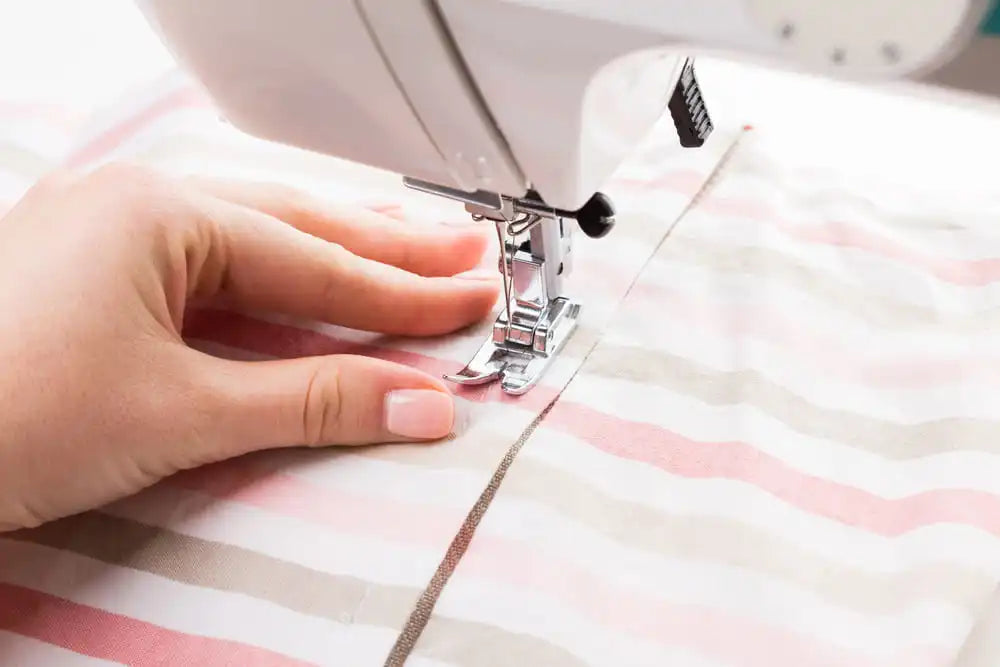 Mains guidant un tissu rayé sous l'aiguille d'une machine à coudre artisanale