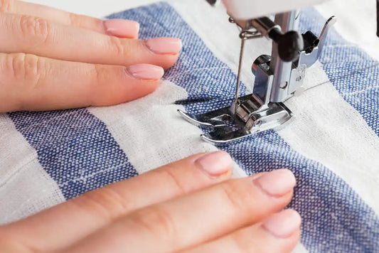 Mains guidant un tissu rayé sous l'aiguille d'une machine à coudre artisanale