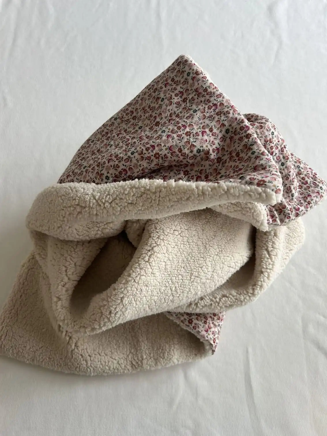 Couverture bébé retournée montrant le sherpa écru bouclé et le coton fleuri rose