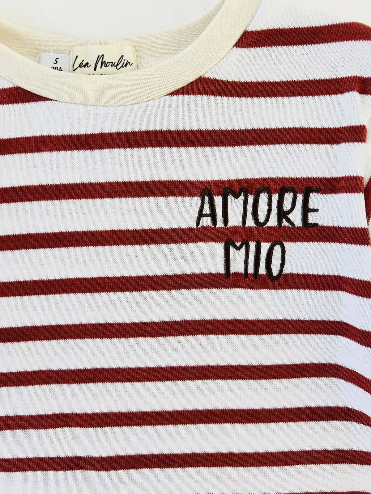 Gros plan sur la broderie noire Amore Mio et le col rond d'un sweat rayé rouge