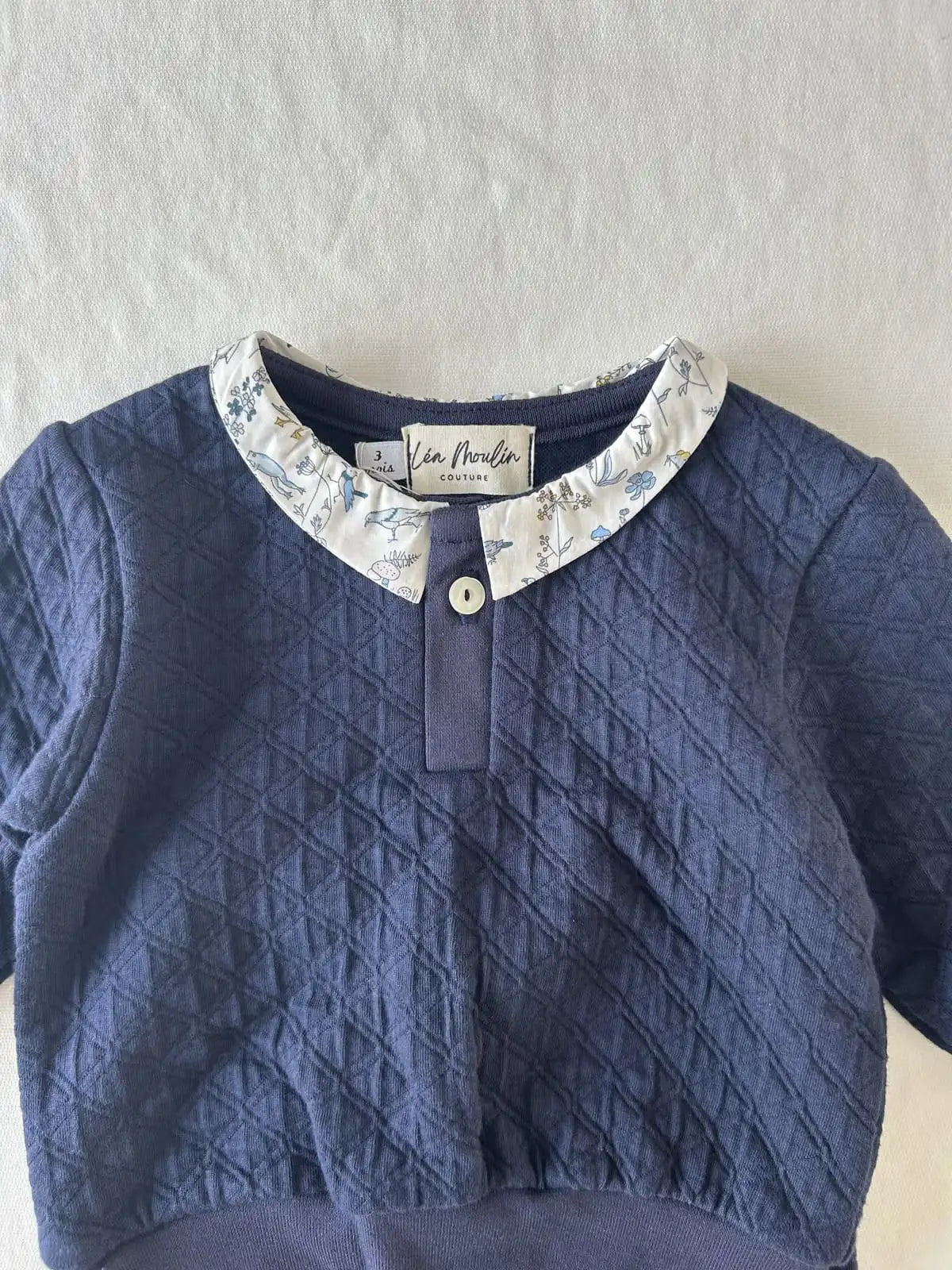 Détail du col en tissu Liberty et bouton unique sur encolure de l'ensemble en coton bleu.