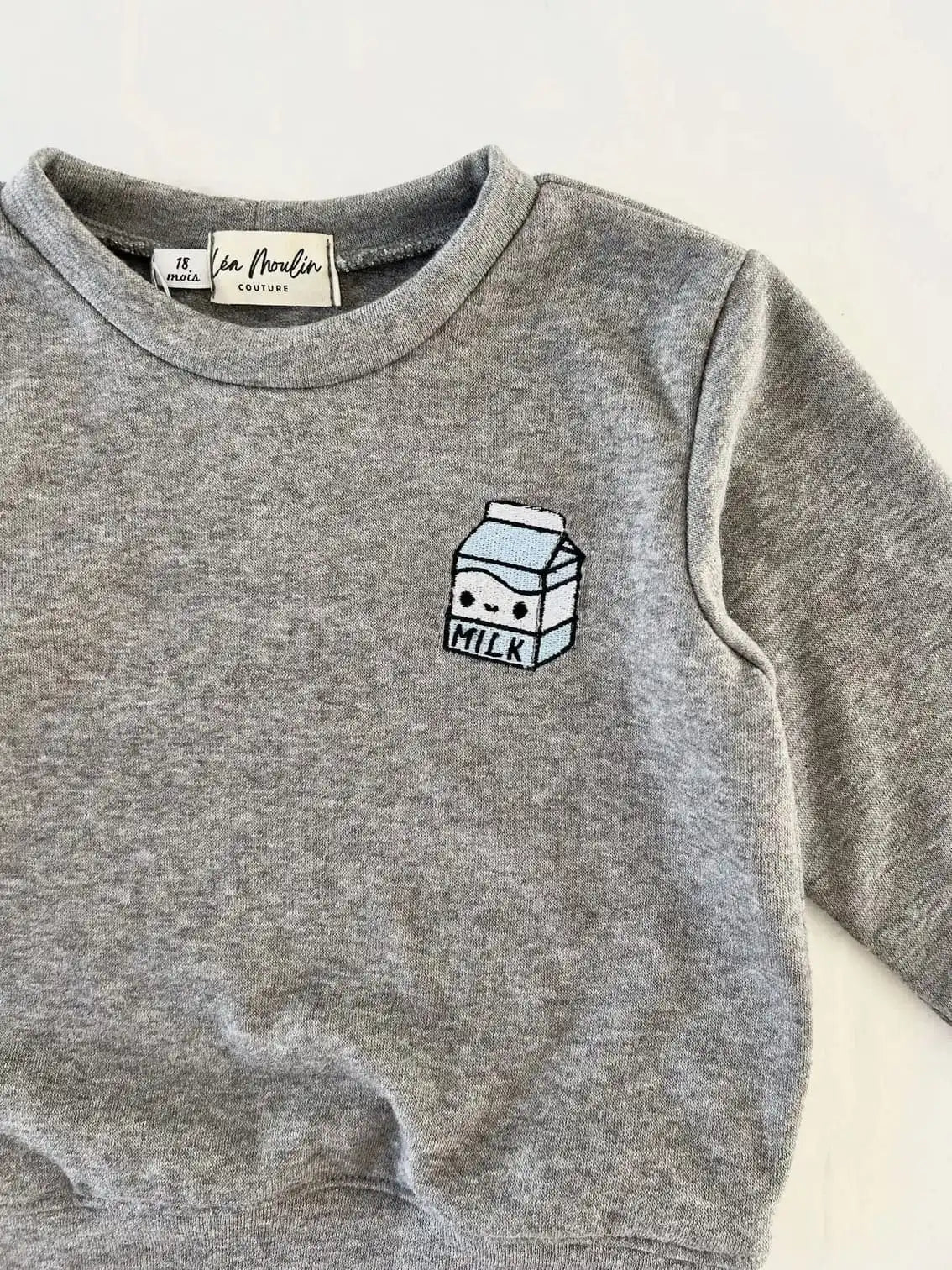 Gros plan sur la broderie brique de lait bleu clair sur le sweat gris chiné