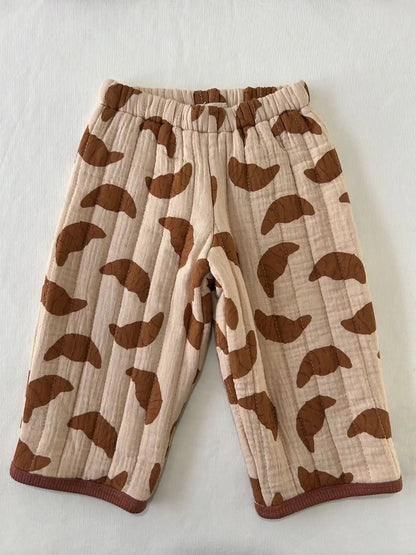 Pantalon large matelassé à motif croissants caramel sur fond beige rosé, vue de face