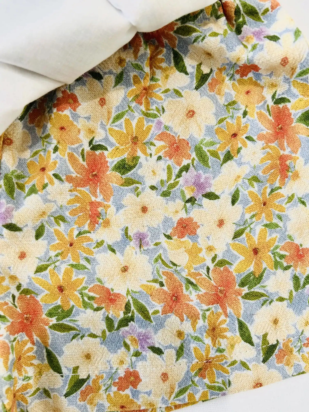Gros plan sur le tissu fleuri viscose et lin de la jupe-culotte bébé fille Agathe, imprimé fleurs jaunes et oranges sur fond écru