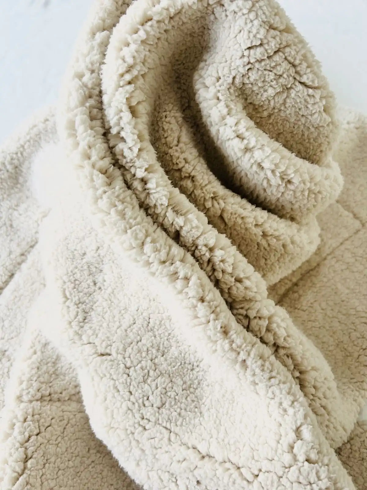 Gros plan sur la doublure en maille sherpa écru ultra-douce et moelleuse de la couverture bébé.