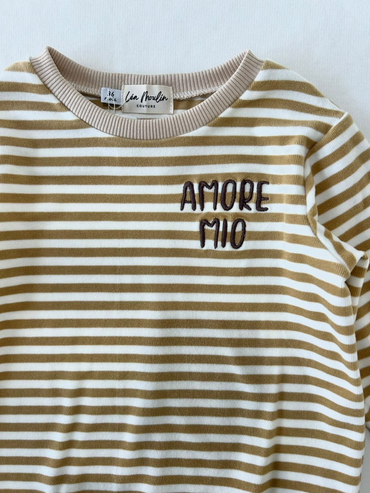 Gros plan sur la broderie Amore Mio et l'encolure extensible d'un sweat bébé rayé jaune moutarde