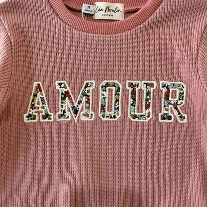 Gros plan sur la broderie Amour en tissu Liberty fleuri du pull bébé vieux rose